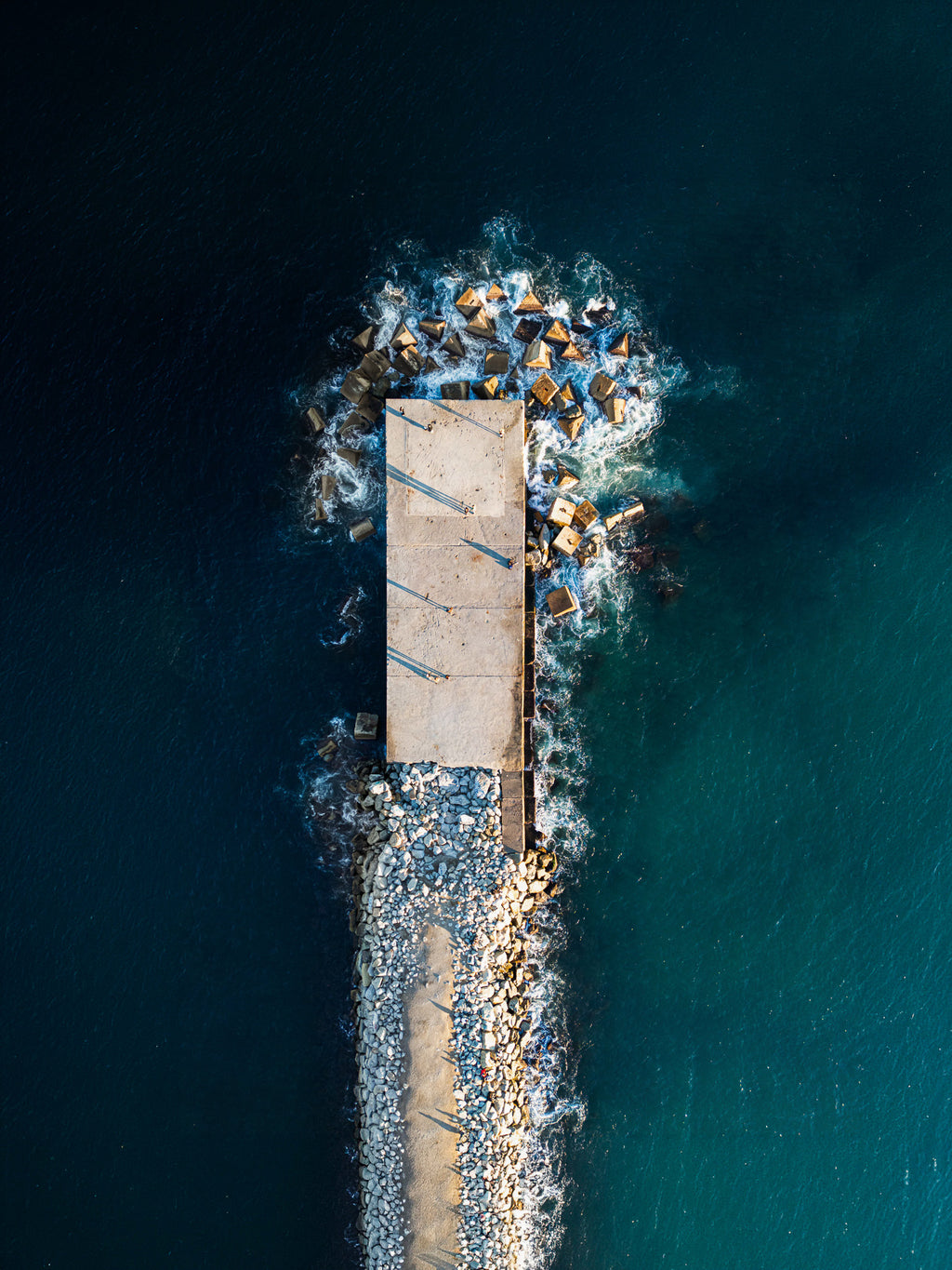 Vista aérea de cima de um quebra-mar de concreto e pedras avançando sobre o mar azul-esverdeado em Barcelona