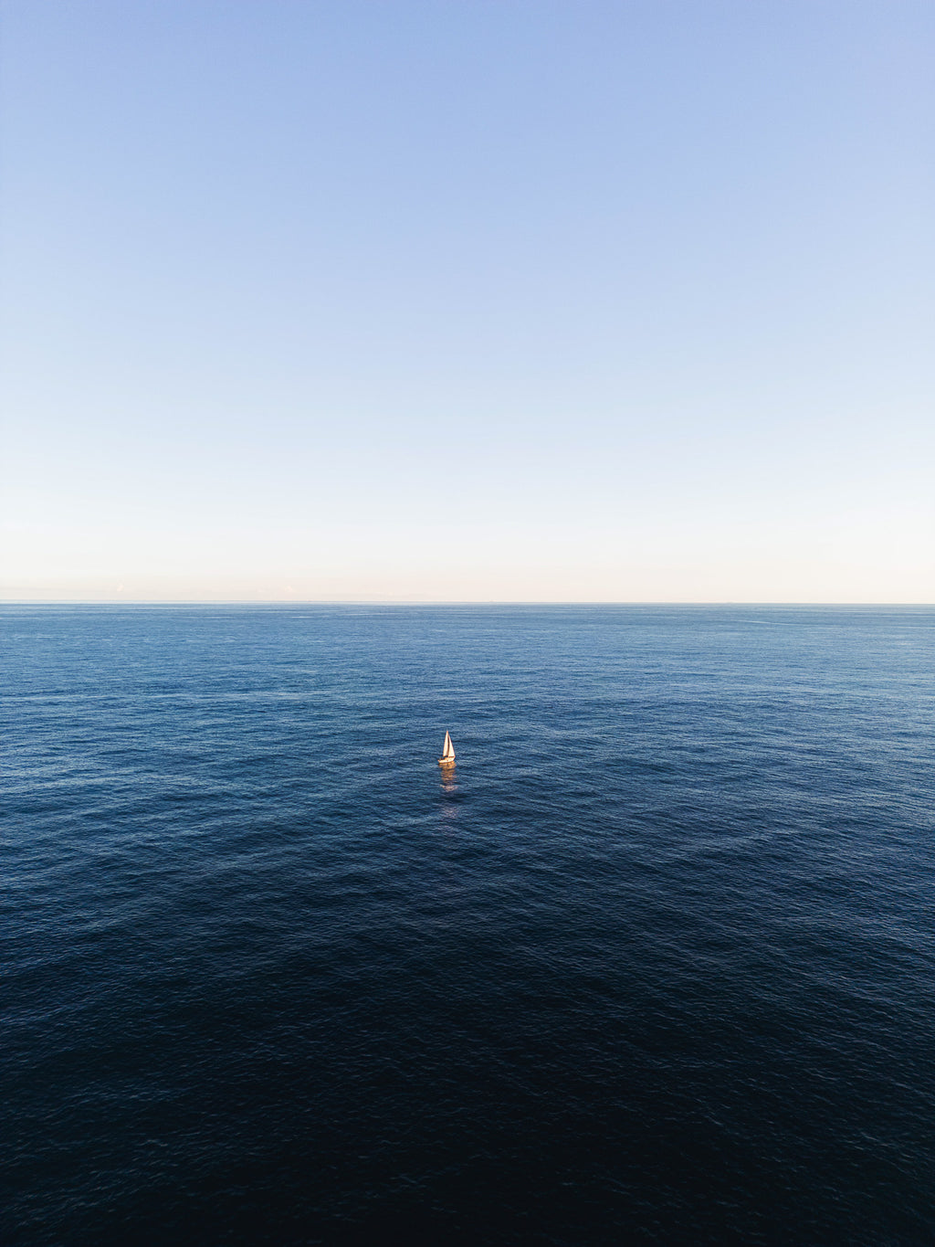 Veleiro branco solitário em mar azul profundo sob céu claro, no litoral de Barcelona