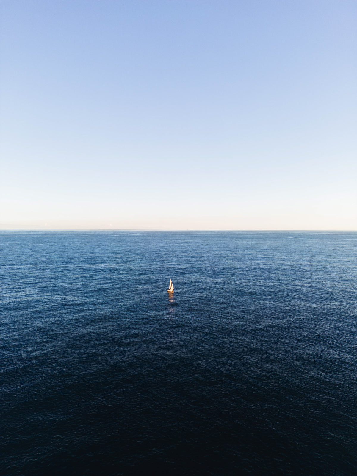 Veleiro branco solitário em mar azul profundo sob céu claro, no litoral de Barcelona